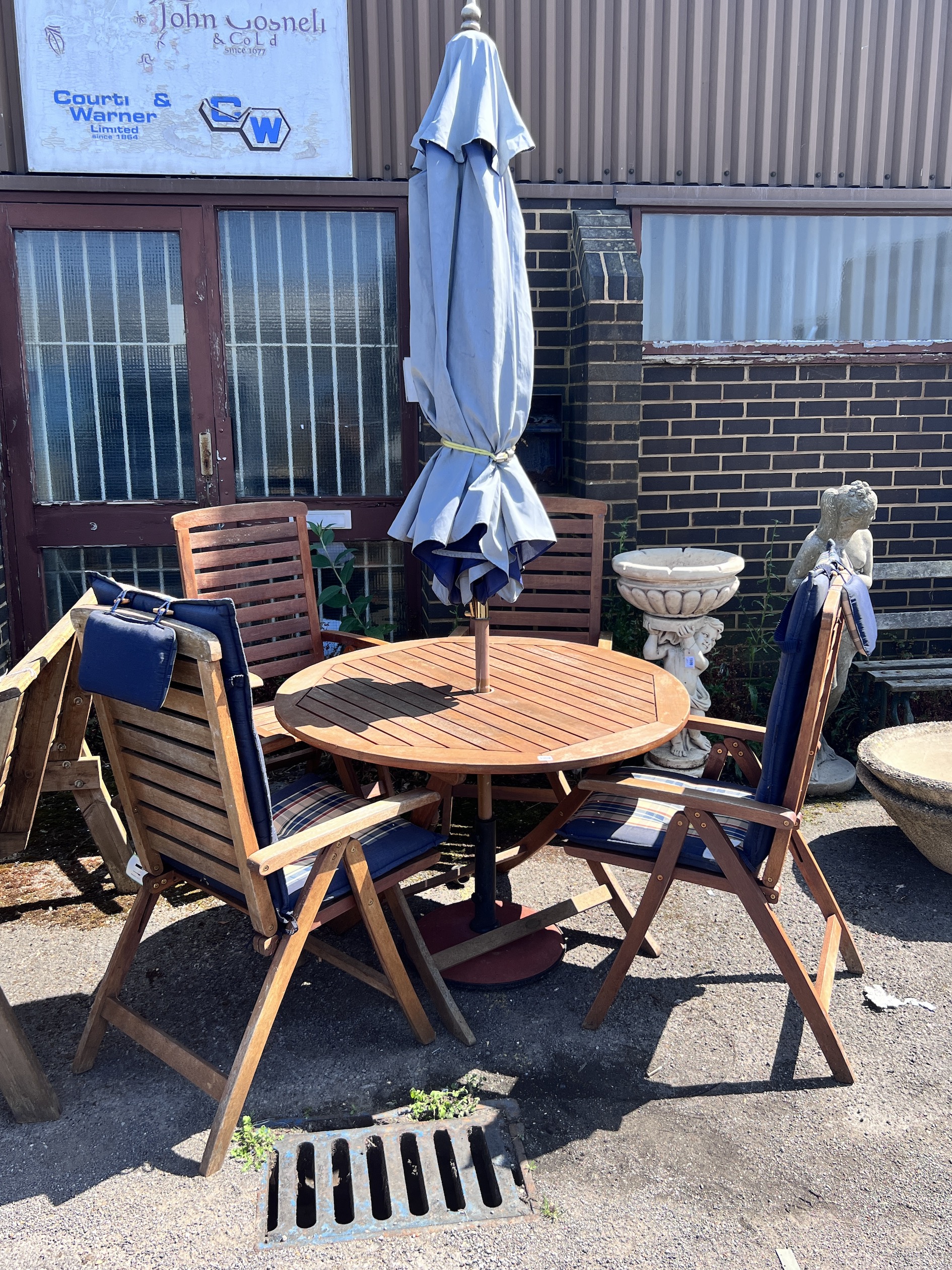 A Royal Craft teak folding table and four chairs with two cushions, parasol and cast metal base, table 110cm diameter, height 74cm.